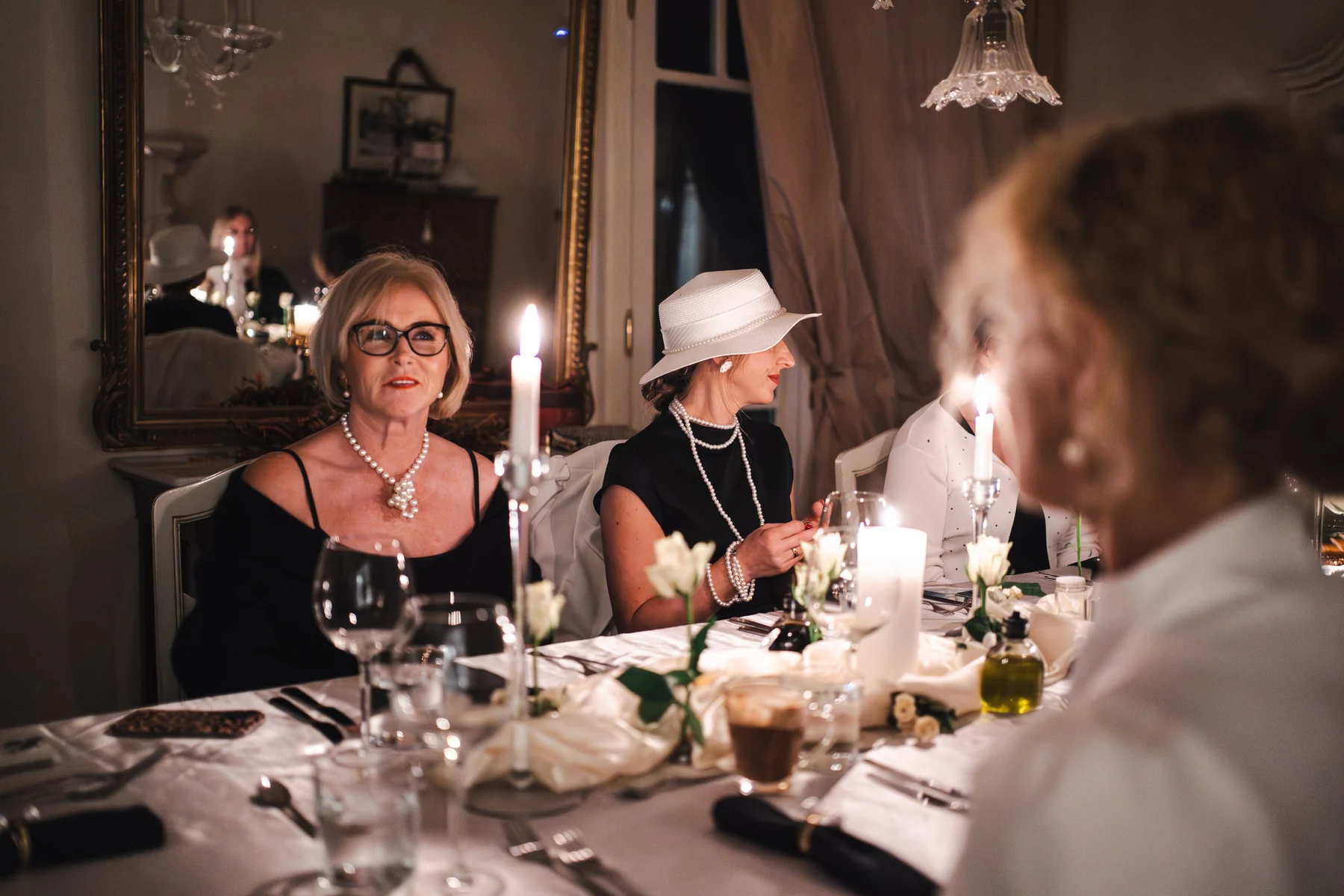 Guests in black-and-white outfits around a celebration table created by Rita in candlelight