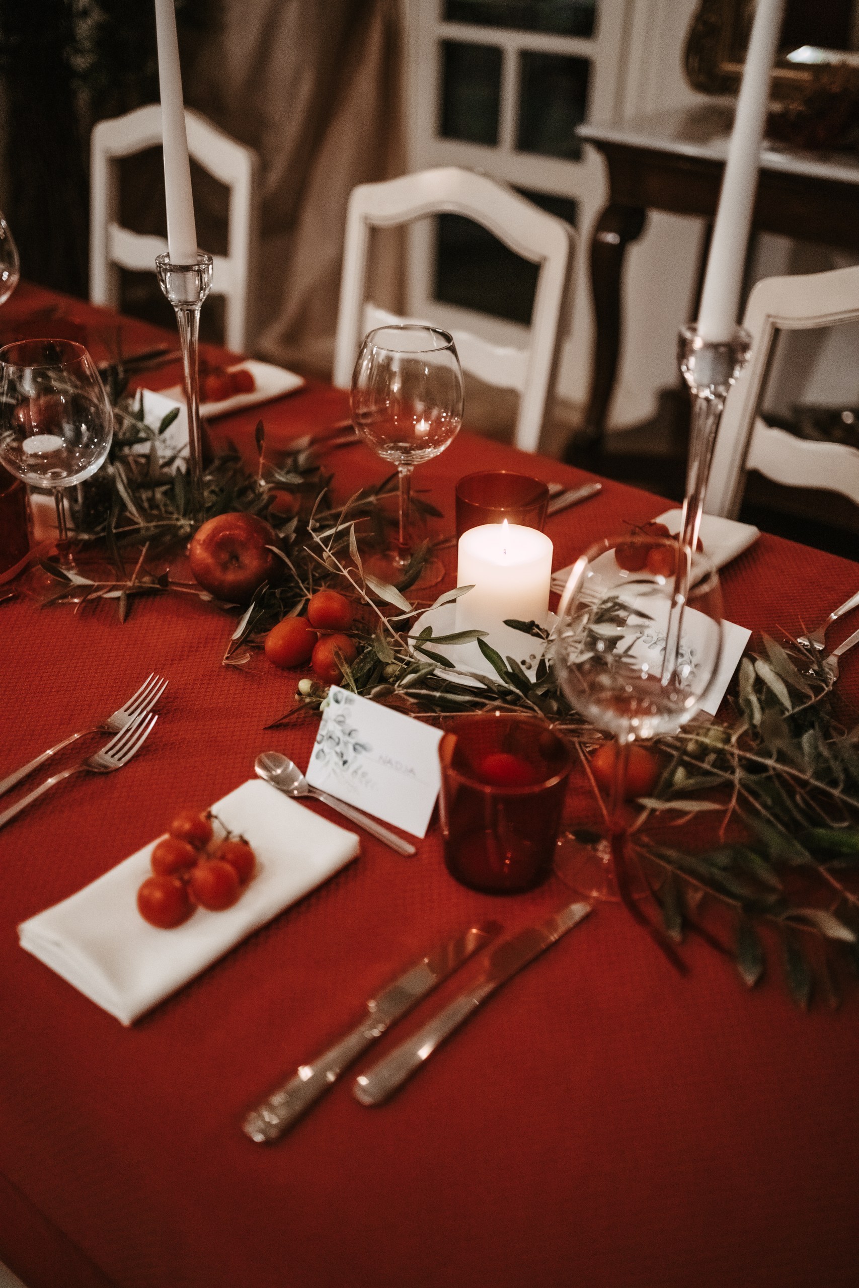 A red celebration table with candles, tomatoes, olive branches and glass details