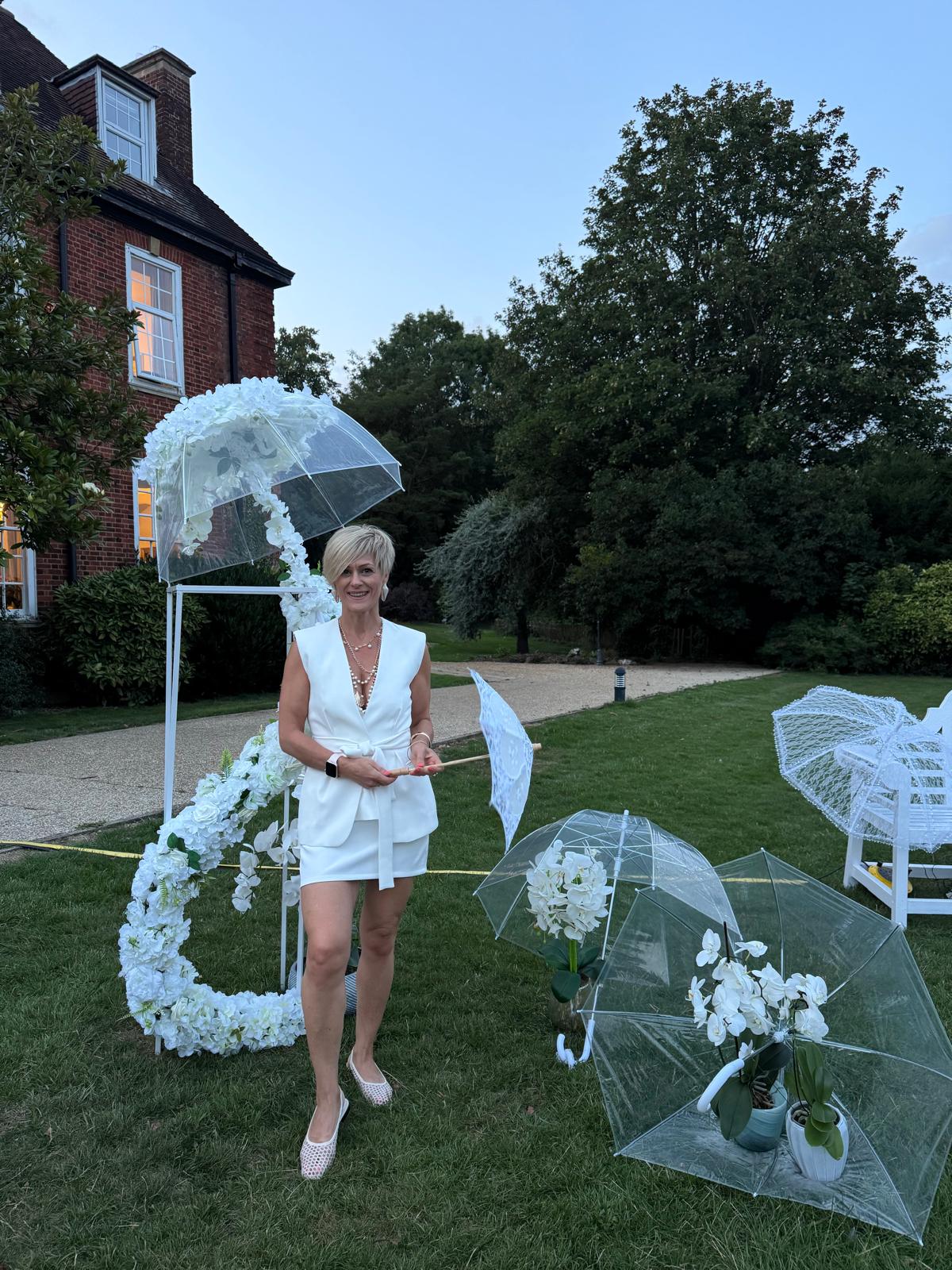 Rita dressed in white beside a white floral and umbrella installation she created