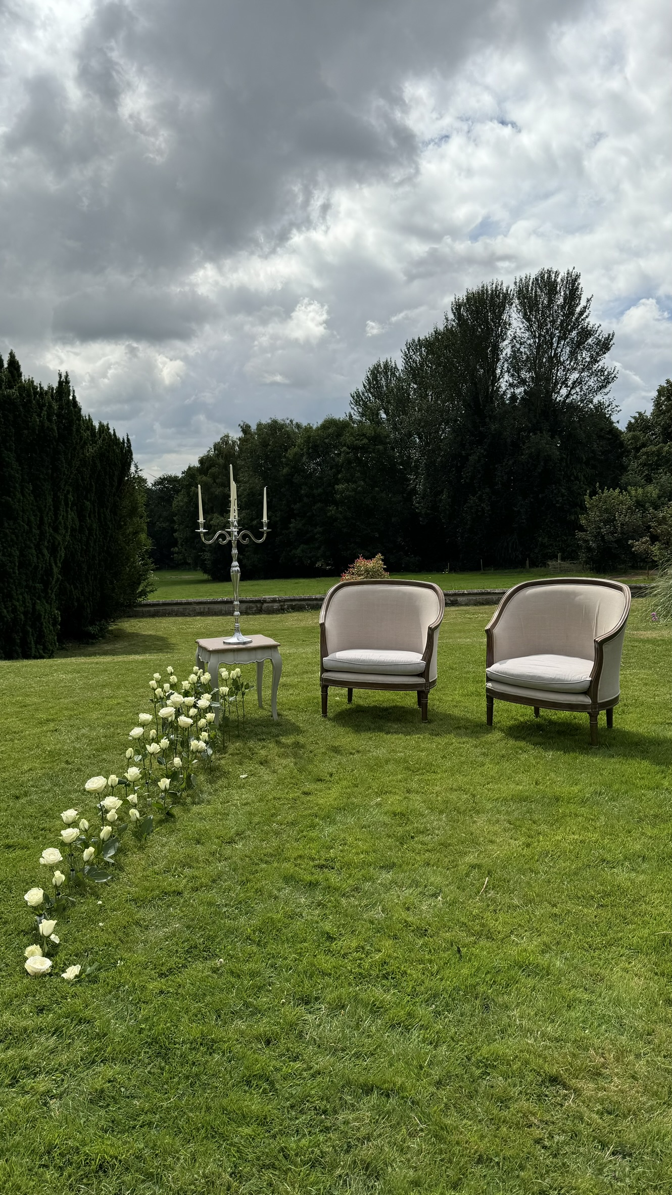 A line of white roses across a lawn leading to chairs and a candelabrum