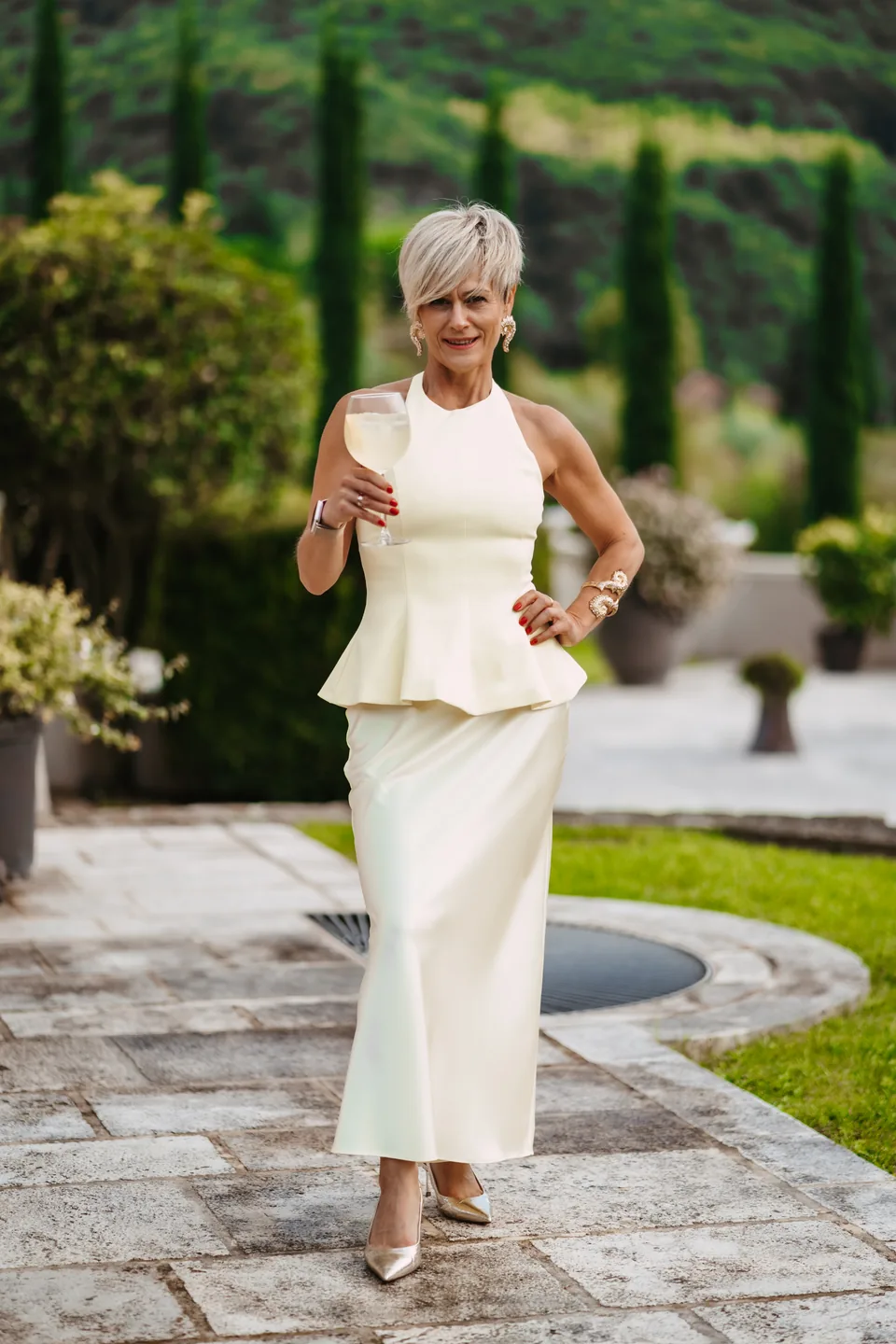 Rita wearing a white occasion outfit in a Tuscan garden.